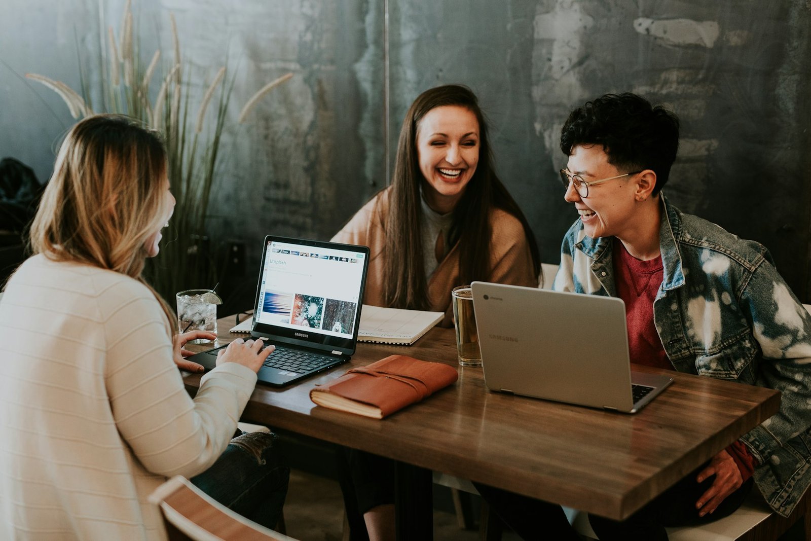 Three people laughing together at a table while working on laptops