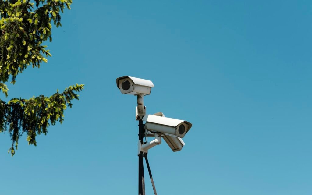 Two white security cameras mounted on a pole against a clear blue sky